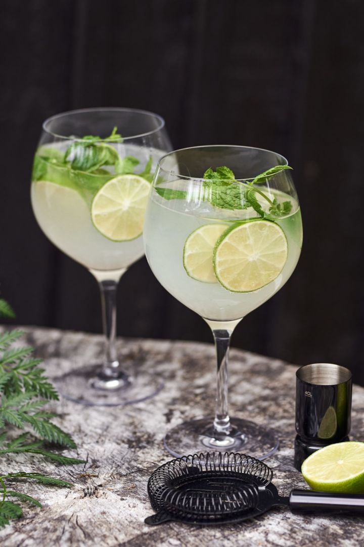 A gin and tonic type of cocktail glass with a cocktail and lime. 