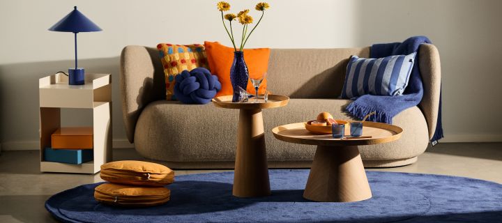 Interior design trends for autumn 2023 are colourful and daring! Here you see blue details like a rug and a lamp in a neutral coloured living room.