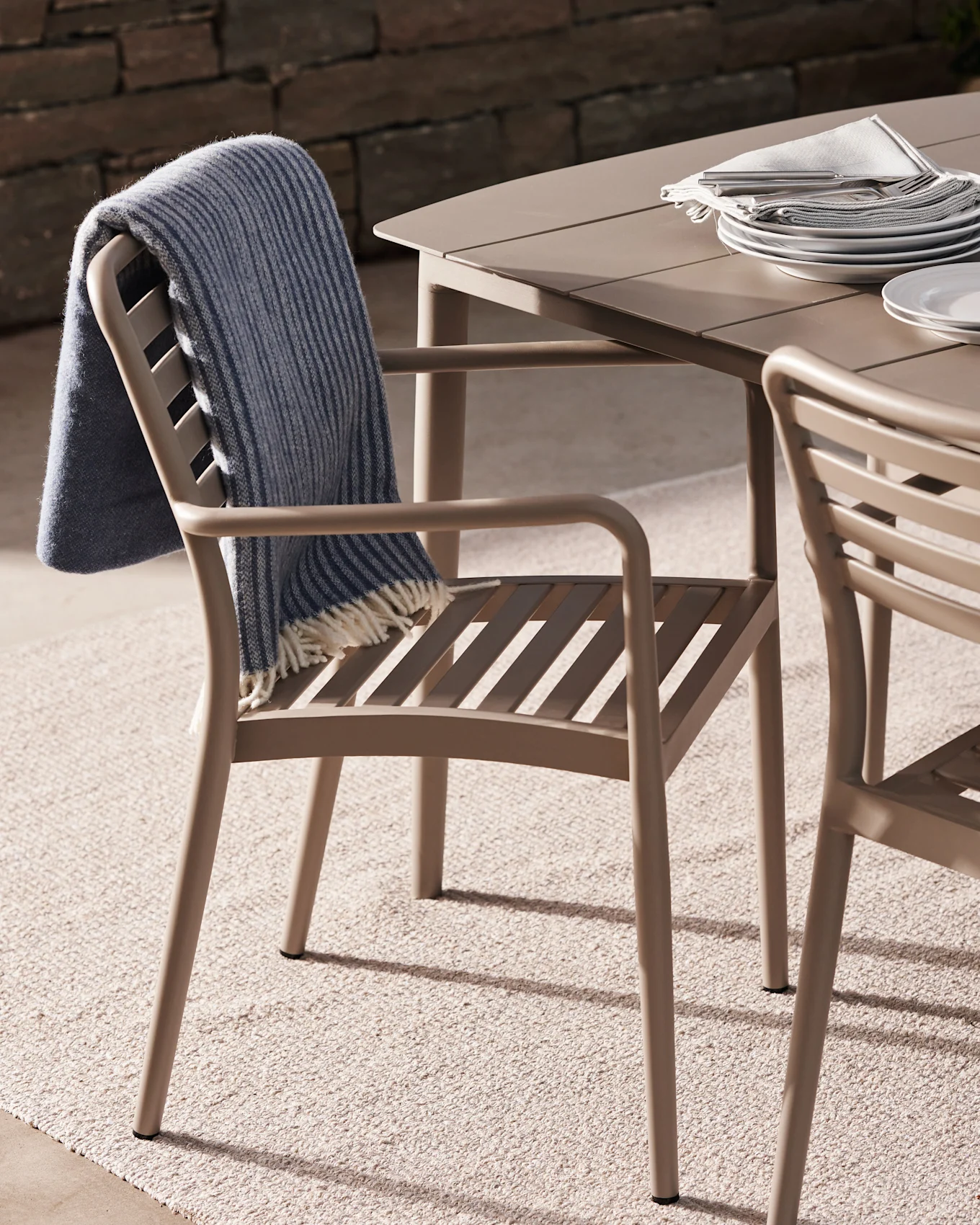 Outdoor dining chair with a blue striped blanket, next to a table set with plates and cutlery on a patio.