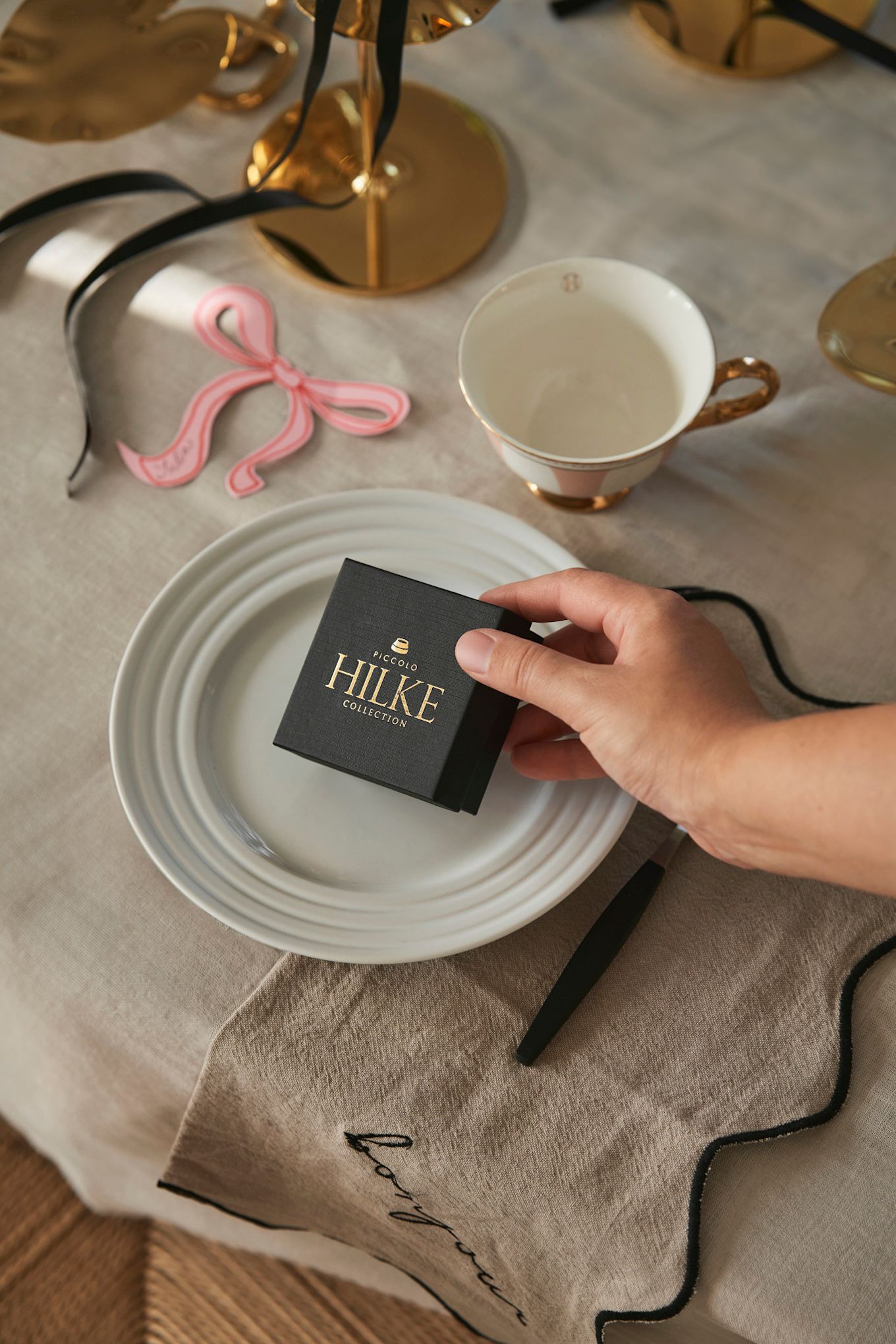 Celebrate Galentine's Day at home with your favourite people. Here you see a hand placing a box from Hilke Collection on a place setting as a small gift for your guests. 