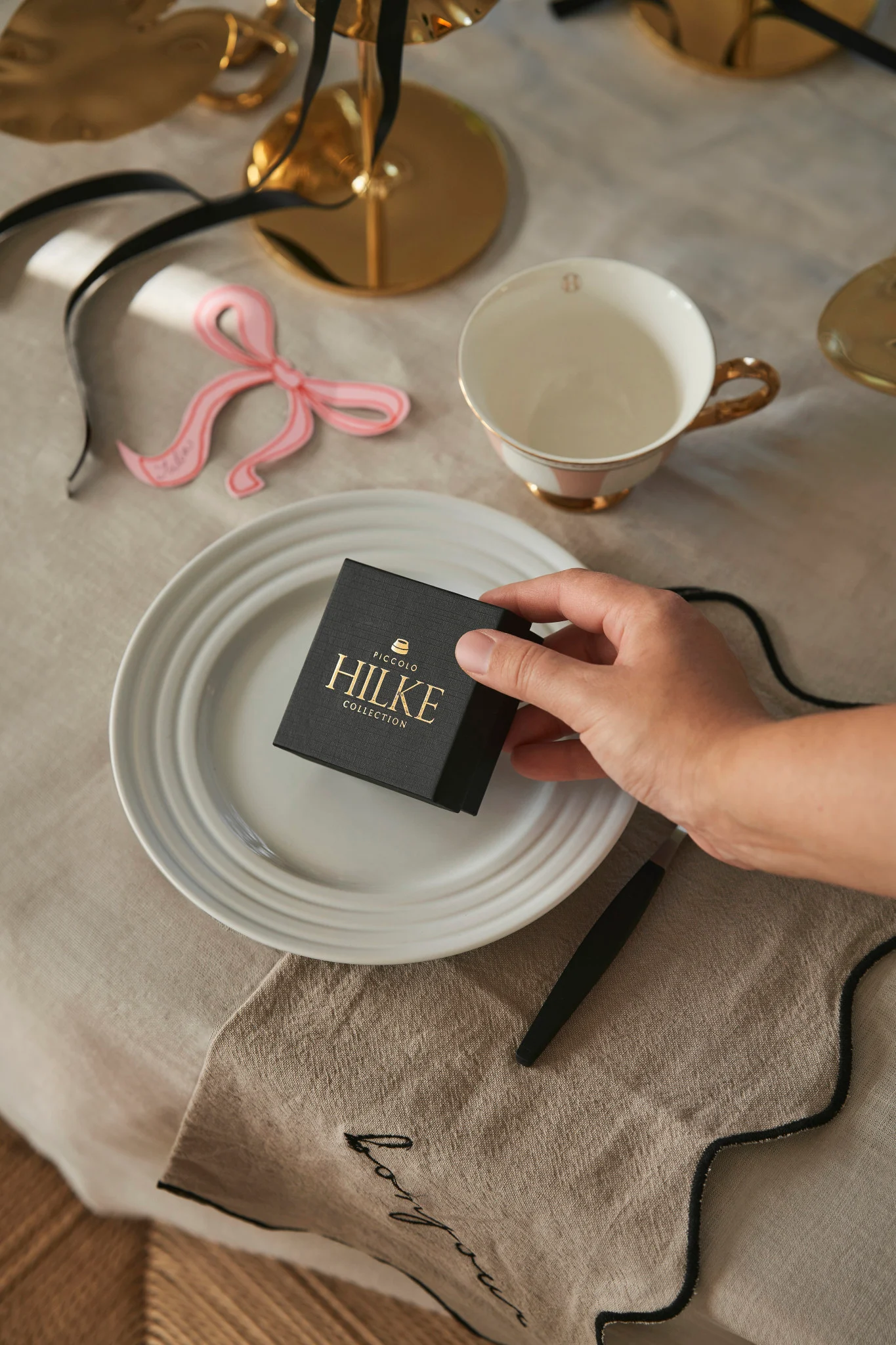Celebrate Galentine's Day at home with your favourite people. Here you see a hand placing a box from Hilke Collection on a place setting as a small gift for your guests.