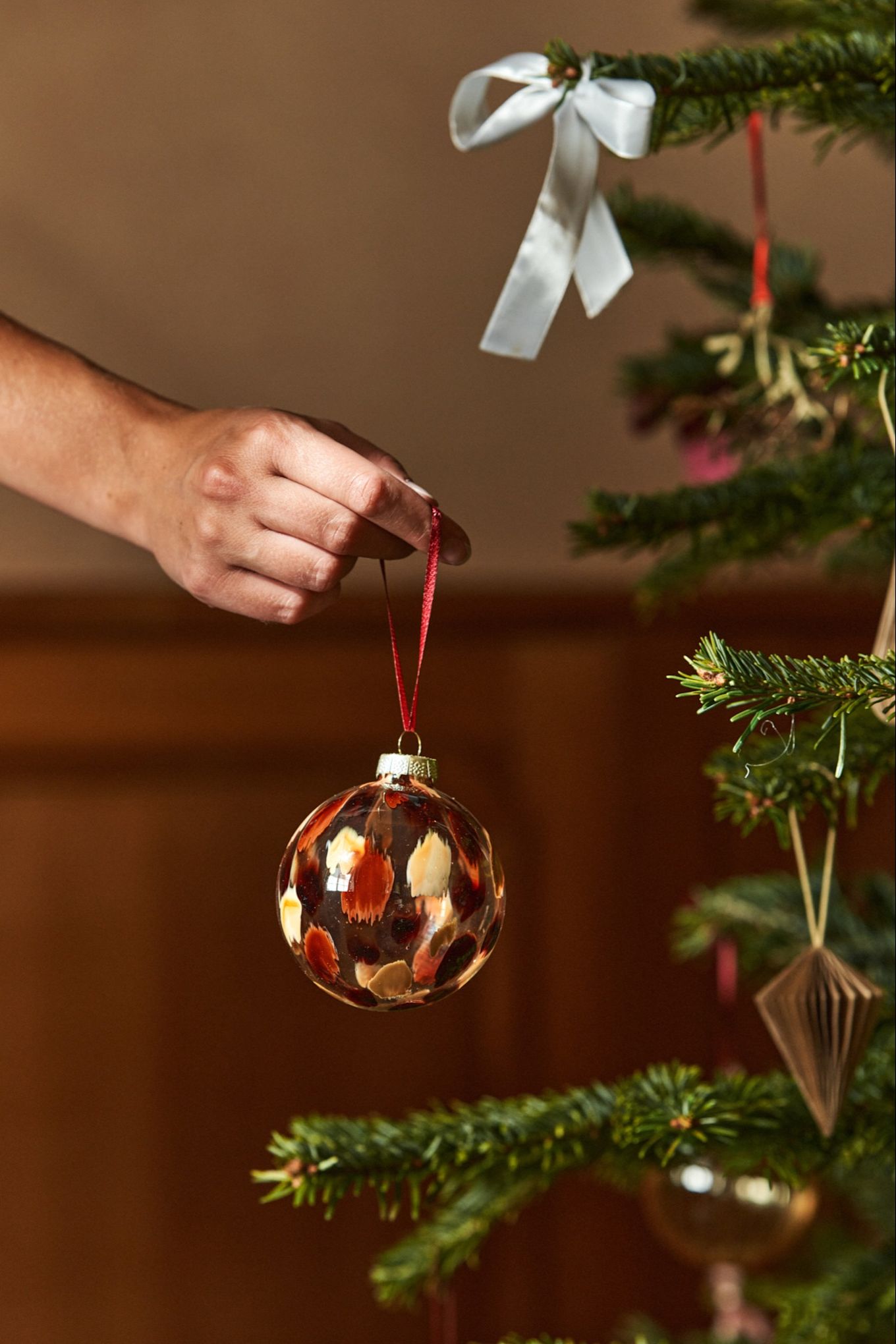 A hand hands a glass bauble in a tree. Glass decorations are as popular as ever for Christmas 2024. 