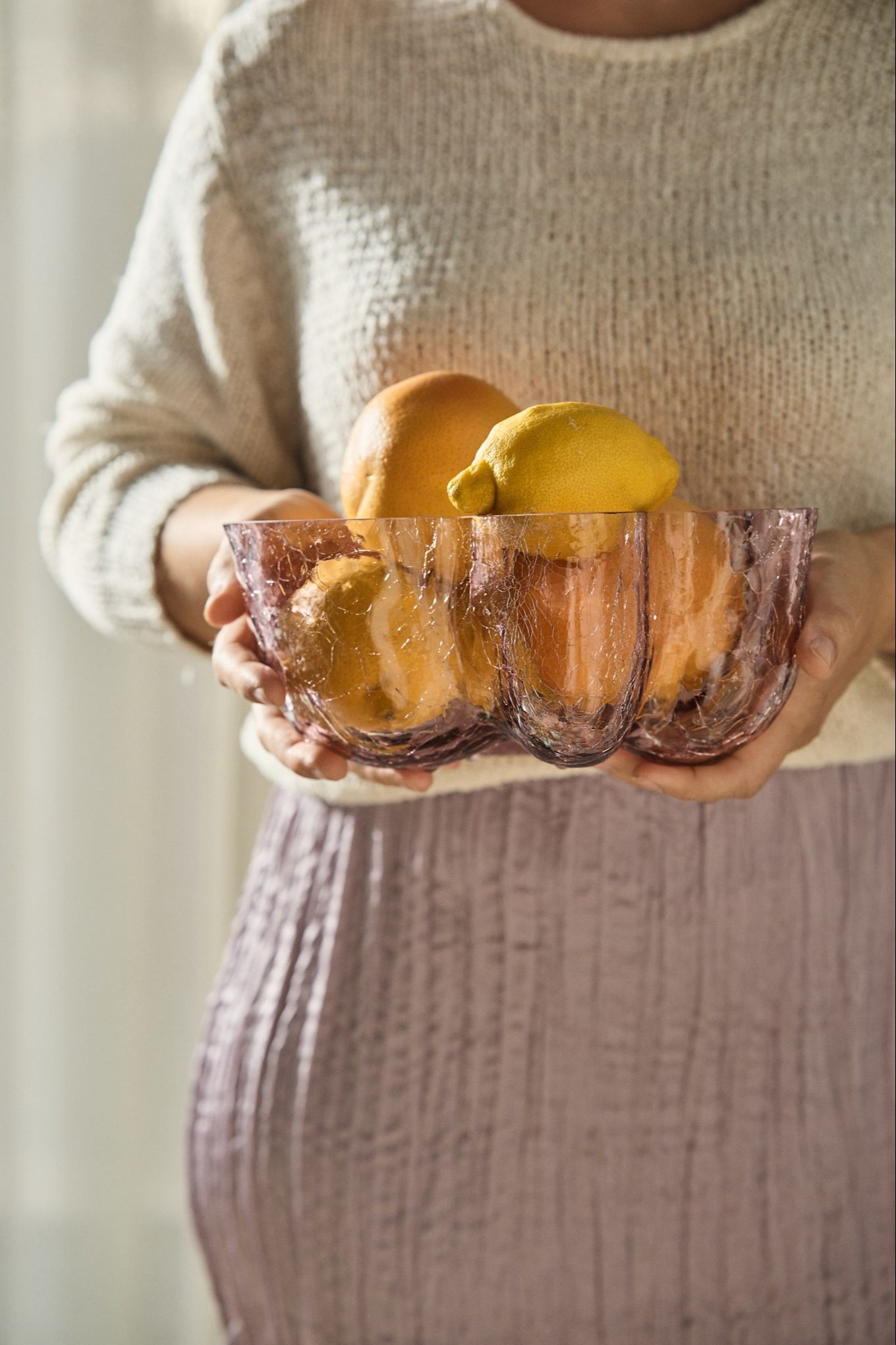 A pair of hands hold a pink glass bowl filled with lemons, coloured glass is one of the interior design trends for autumn 2024. 