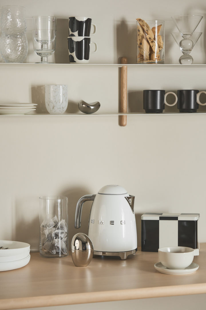 Have a kettle handy in your coffee bar, like this one from Smeg, which stands here in a coffee corner, surrounded by a shelf with various cups and boxes.