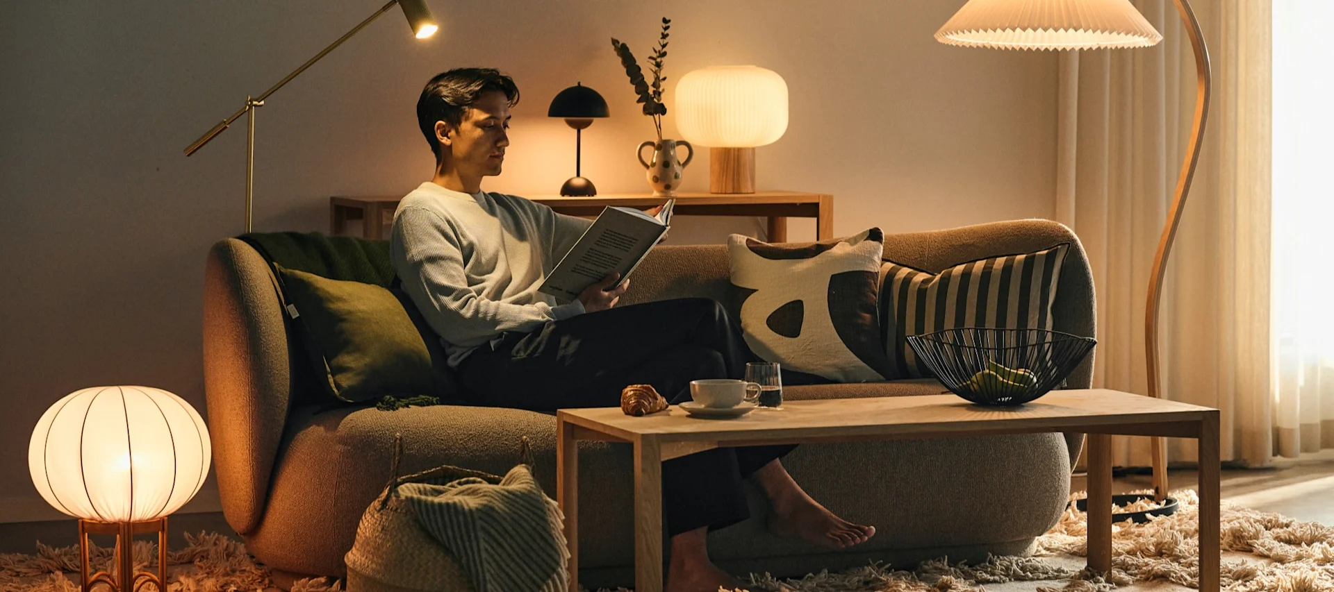 Choosing the right light bulb is important for the feeling in your home - a man sitting on a sofa surrounded by different light sources, reading a book.