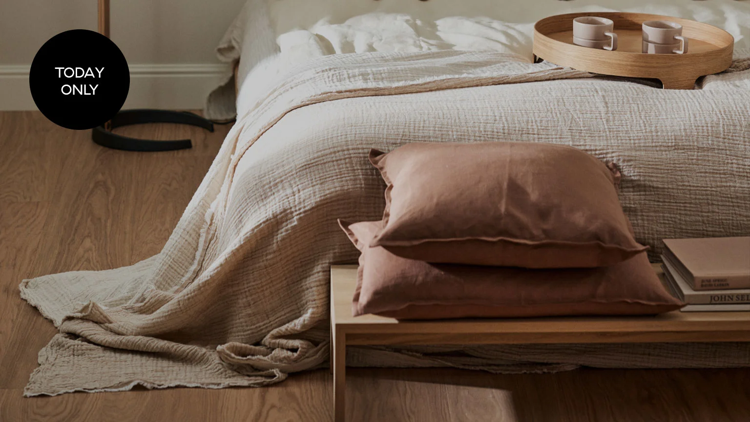 A bed with light-colored, textured bedding, two rust-colored pillows on a bedside table, and a 'Today Only' tag.