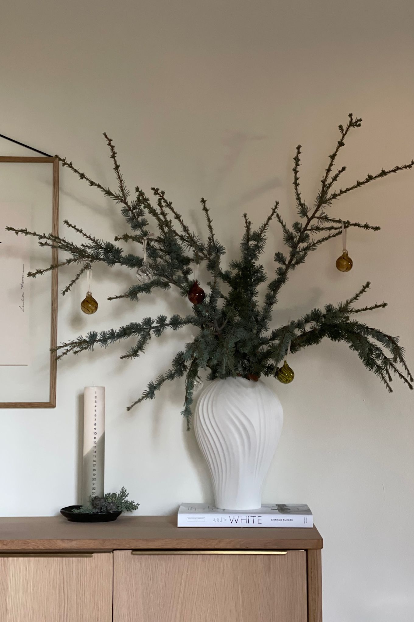 Minimalist Christmas decor uses natural materials, pine cones and branches, and a neutral colour pallet like these branches in a vase along side an advent candle. 