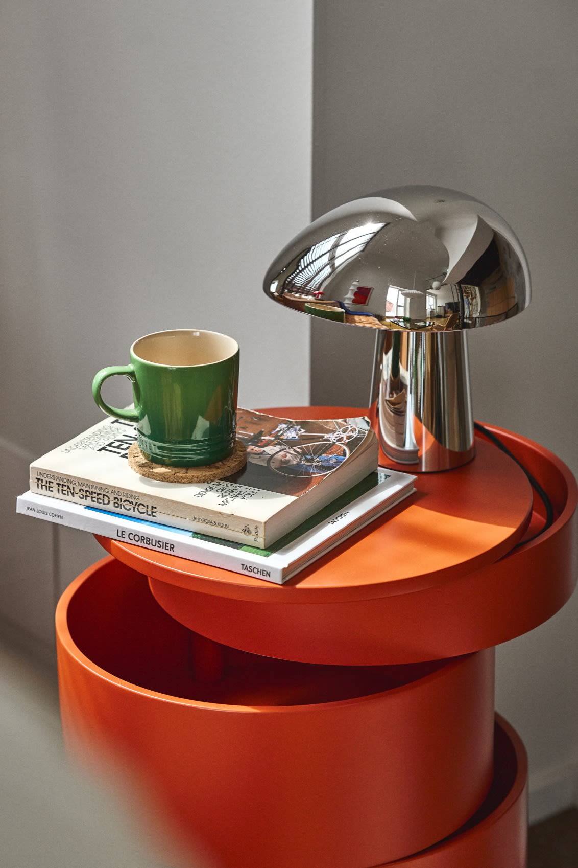 Give your home an update with these modern lighting ideas like the Night Owl lamp from Fritz Hansen in chrome seen here on a red bar table with some books and a green mug. 