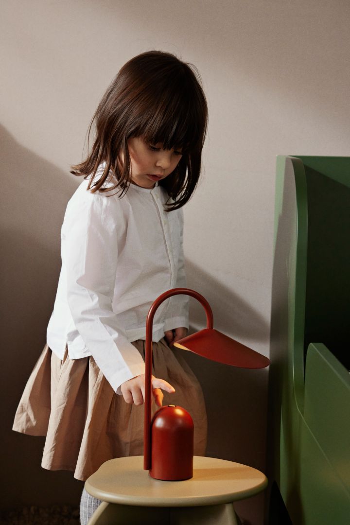 A child presses the switch on the red portable lamp Arum from ferm LIVING. Portable lighting is a great idea for a children's room. 