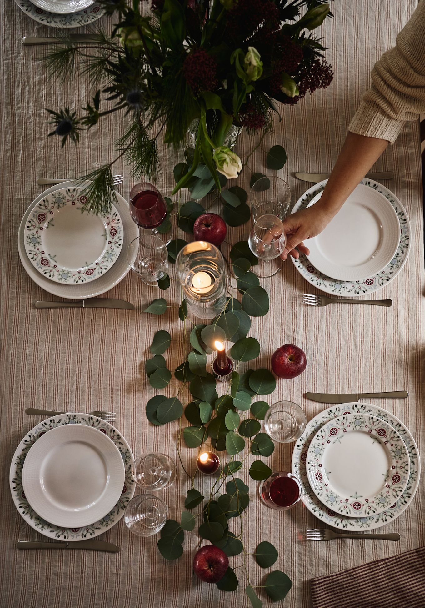 A simple and elegant Christmas table setting idea photographed from above with green leaves and red apples for decoration. 