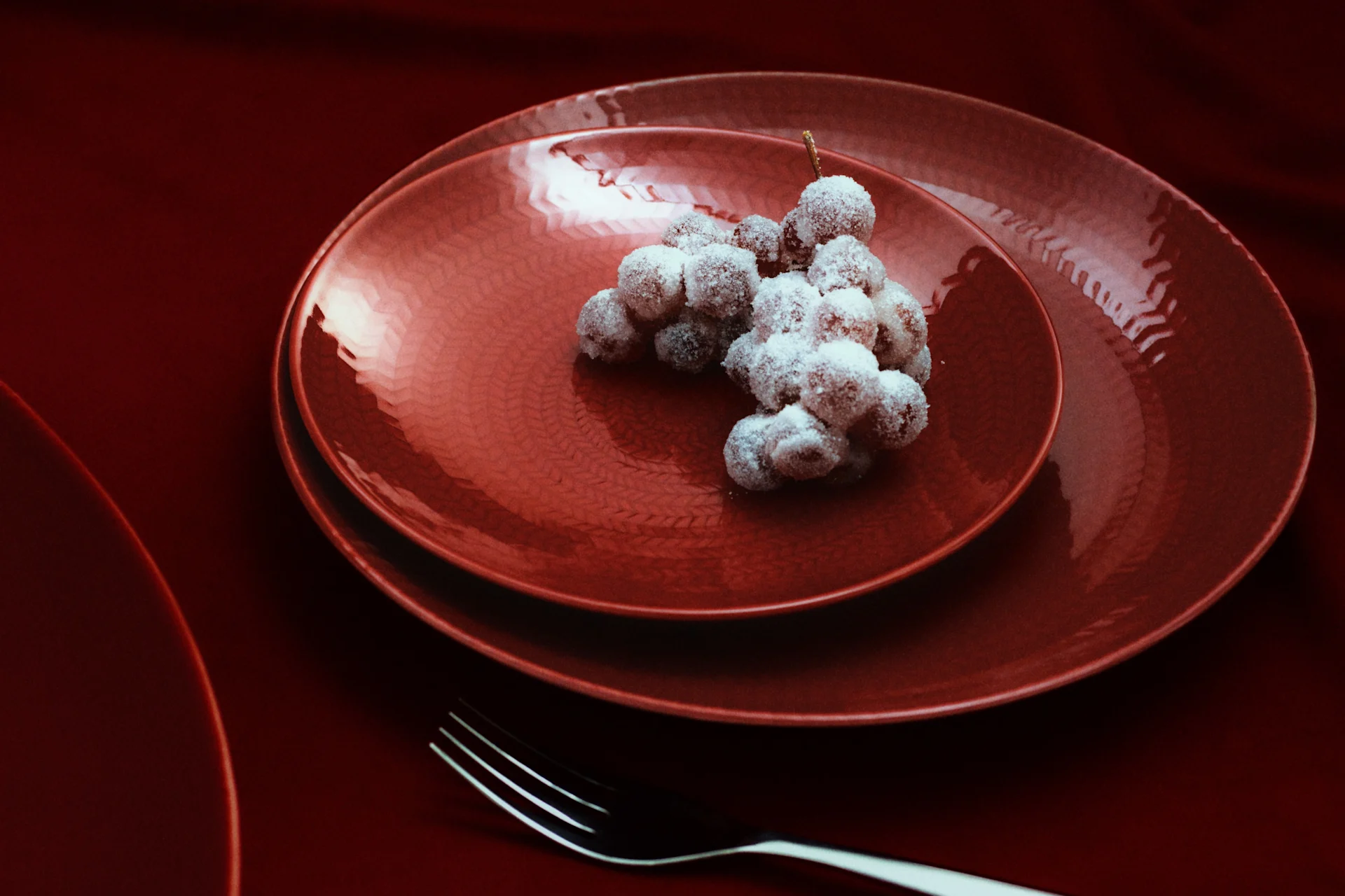 Sugared grapes on red textured plates with forks on a dark red table setting.