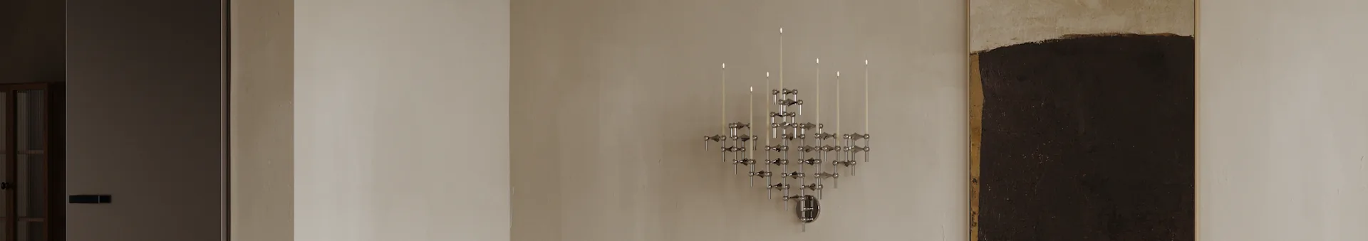 A geometric chrome modular candle holder with several lit white candles mounted on a light wall in a modern room.