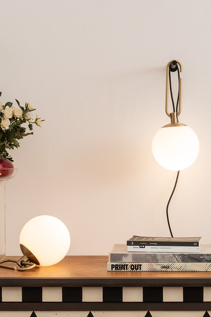 The NH wall and table lamps from Artemide hang and stand on a desk with a stack of books.