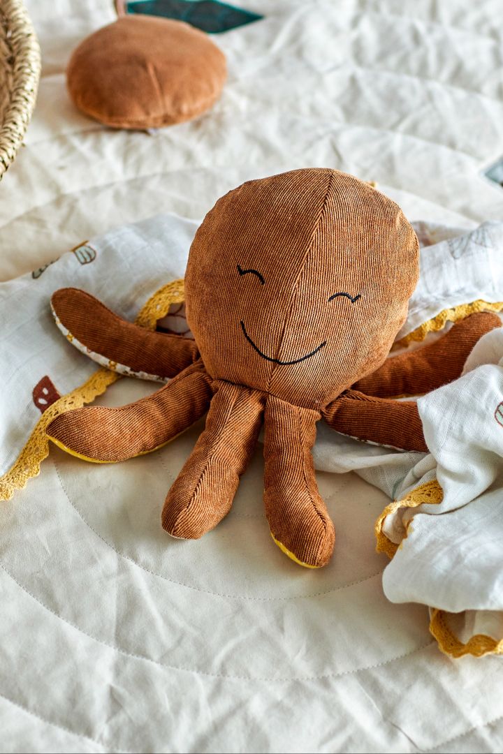 A smiling octopus soft toy lays on a quilted floor mat. Soft toys are the perfect baby shower gift idea for the little one. 