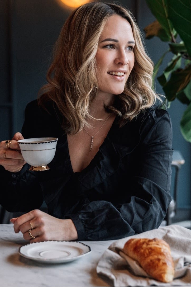 Founder Giovanna Hilke sits at a table and looks to the side. She is holding the Lignano Sabbiadoro cup from Hilke Collection in her hand.