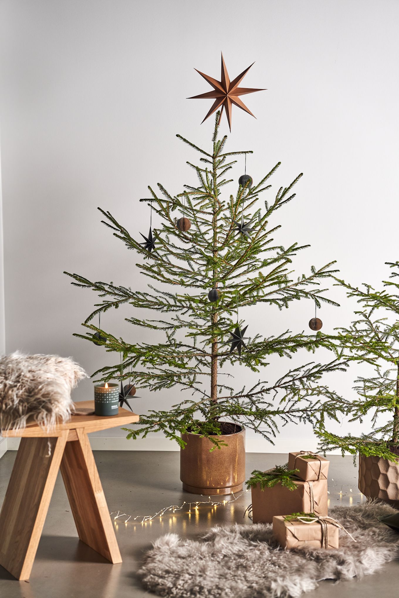 Decorate the Christmas tree with Christmas tree decorations for 2021 in 4 different styles according to Nest Trends - Nurture, Share, Boost and Cultivate. Here you see Angle stool from Muubs with A Skandinavisk scented candle in the Forest scent next to packages on a sheepskin rug. 