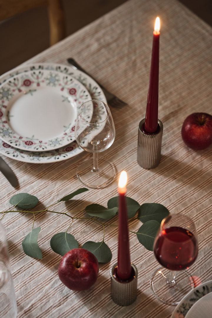 A close up image of deep red candles in chrome candle holders as part of a simple Christmas table setting. 