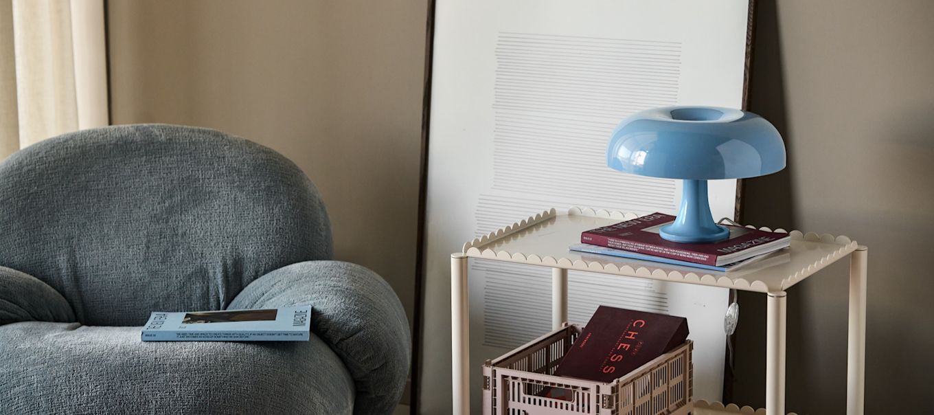 The Nessino mushroom lamp stands illuminated on a desk with pens, books and a plant. 