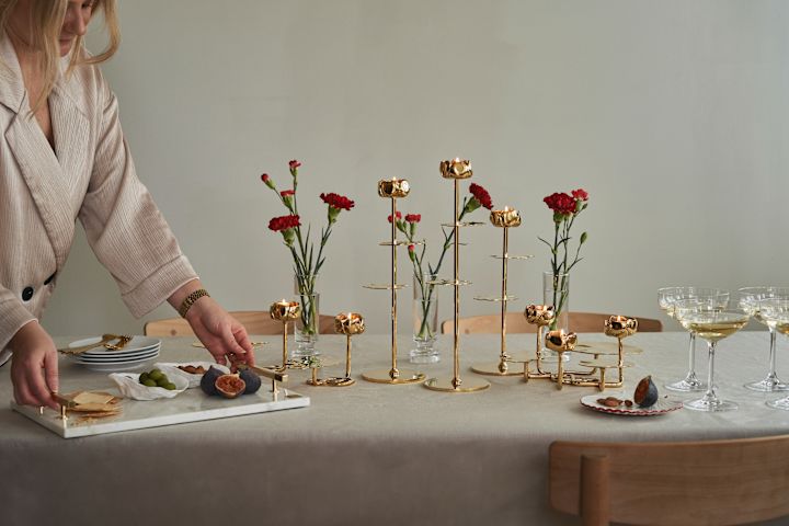 Elegantly set tables are what we like to pick up from Scandinavian interior design trends 2025. Here with brass candlesticks from Hilke, red flowers and linen tablecloth.