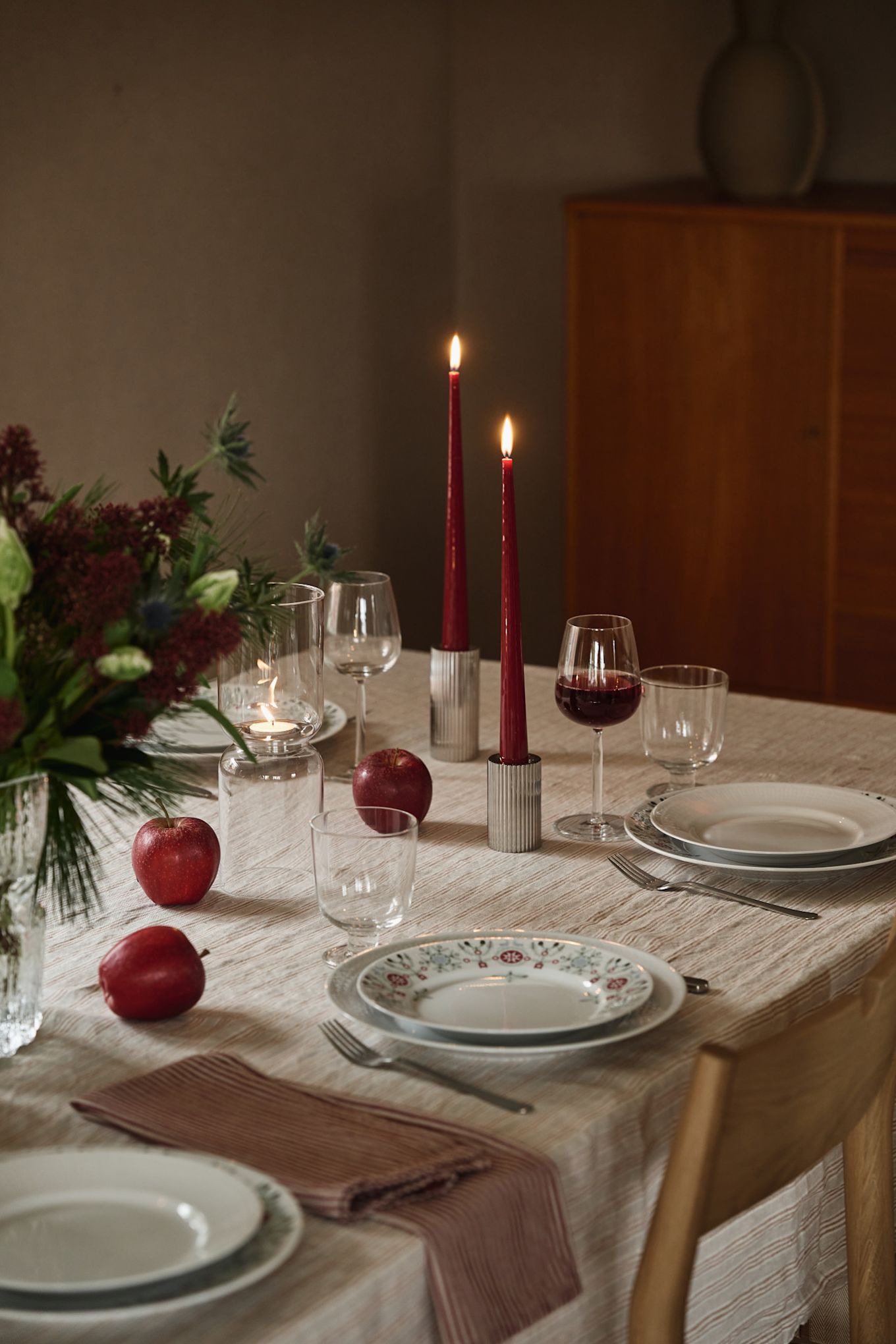 Red Christmas candles stand on a simple Christmas table setting with patterned plates and red accents. 