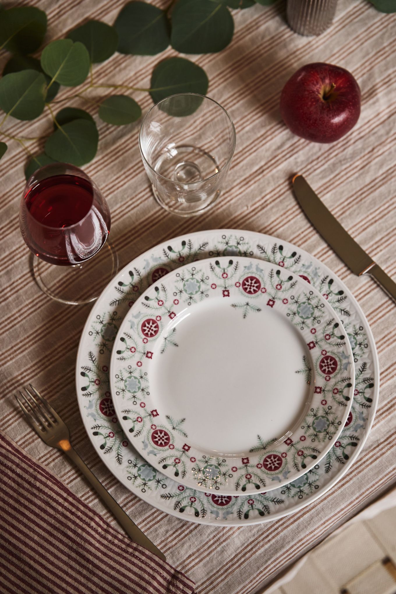 An overhead image of a set of Christmas plates in a simple Christmas table setting idea. With a striped tablecloth and simple natural table decorations. 