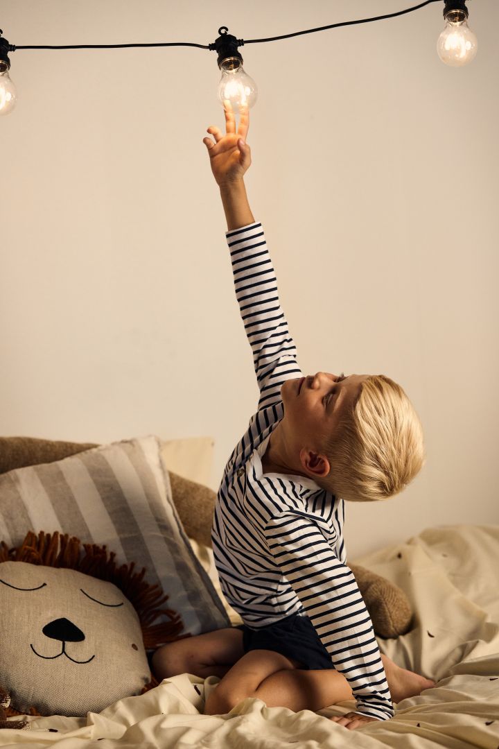 A boy reaches for a light on a string of lights in children's room. String lights are the perfect decorative lighting for a children's bedroom. 