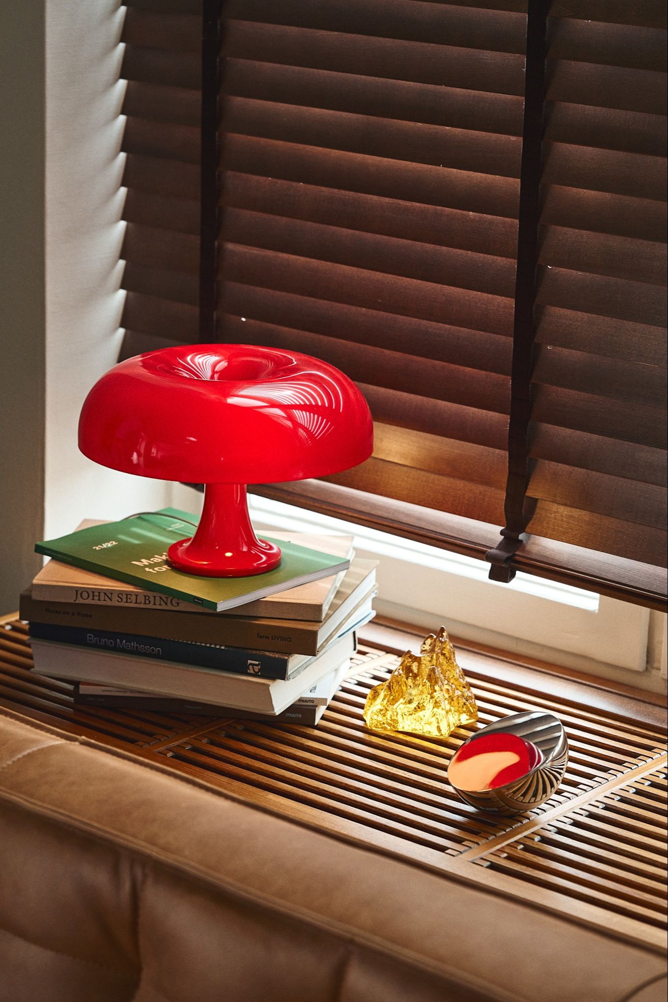 The Nessino mushroom shaped lamp in red stands on a stack of books on a windowsill. 