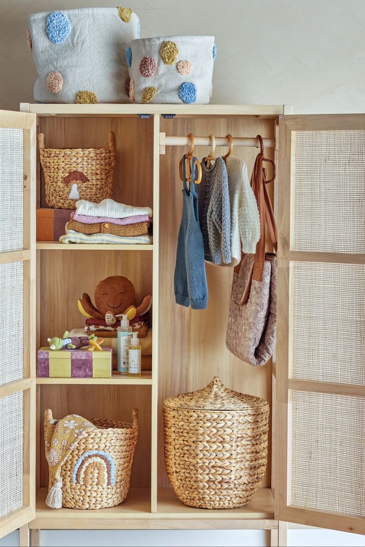 A wooden wardrobe filled with plaited wicker storage baskets and children's clothes. Storage baskets are a great baby shower gift idea. 