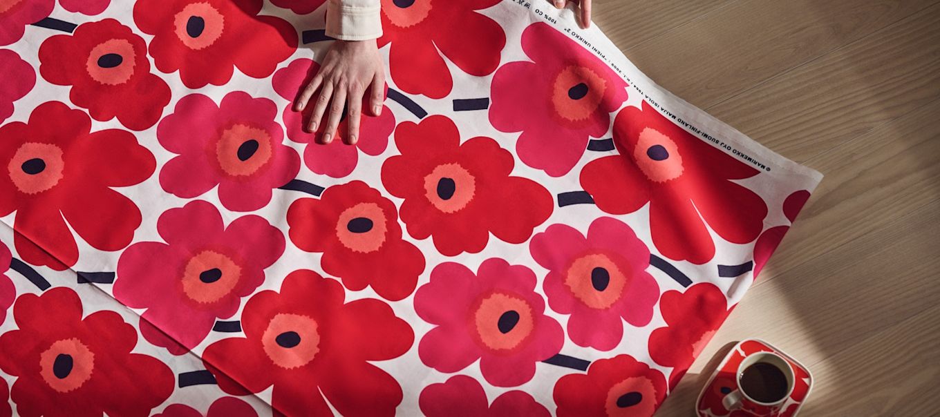 A hand rests on a bright red sheet of Unikko fabric from Marimekko. 