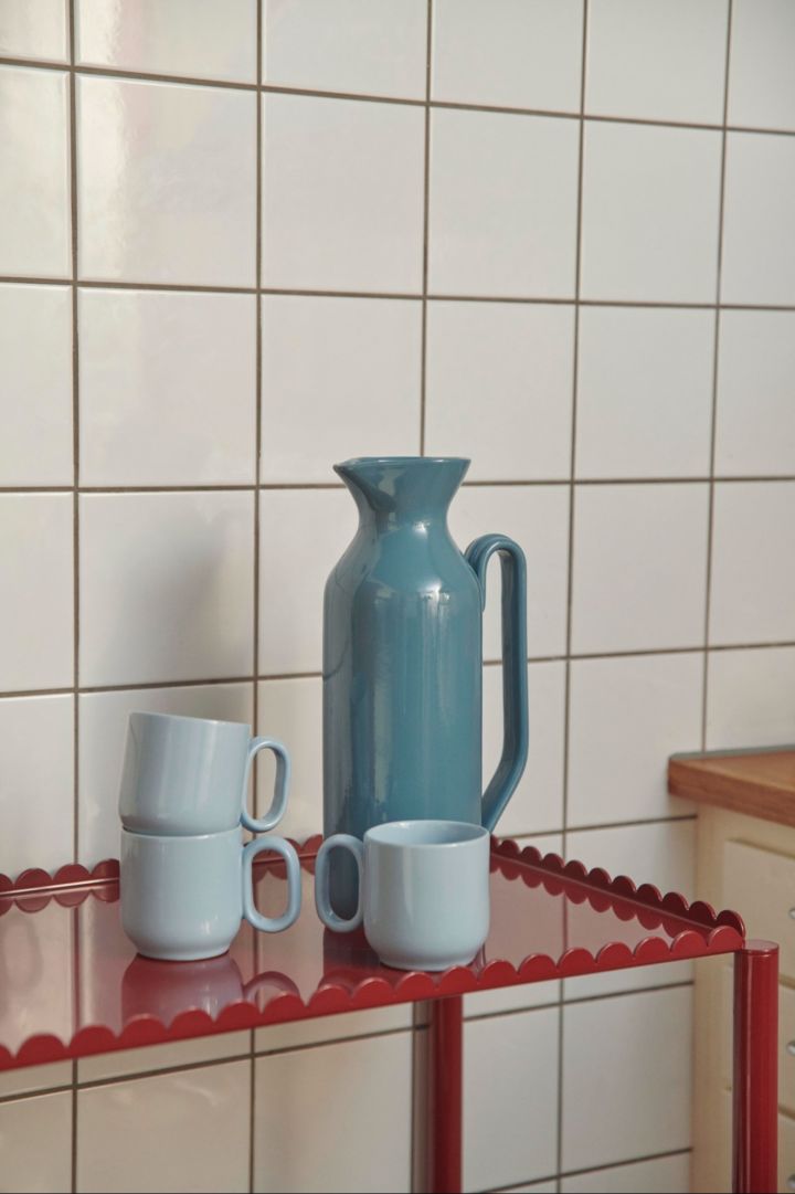 Scalloped edges bring a sweet touch to the autumn interior design trends 2024, here you see the Arcs trolley in red with the Barro jug in dark blue and three Barro mugs in light blue.  