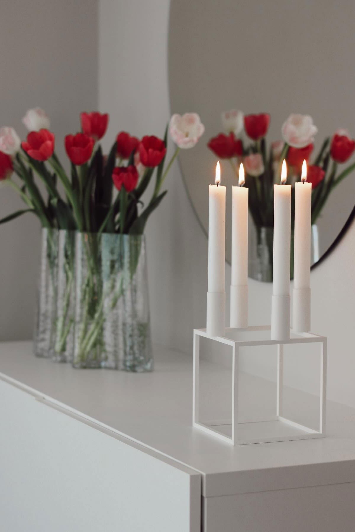 Here, the white Kubus candle holder with four candles from Audo Copenhagen stands on a chest of drawers, behind it the Gry vase from Cooee Design with tulips in @susannfrustol's home.