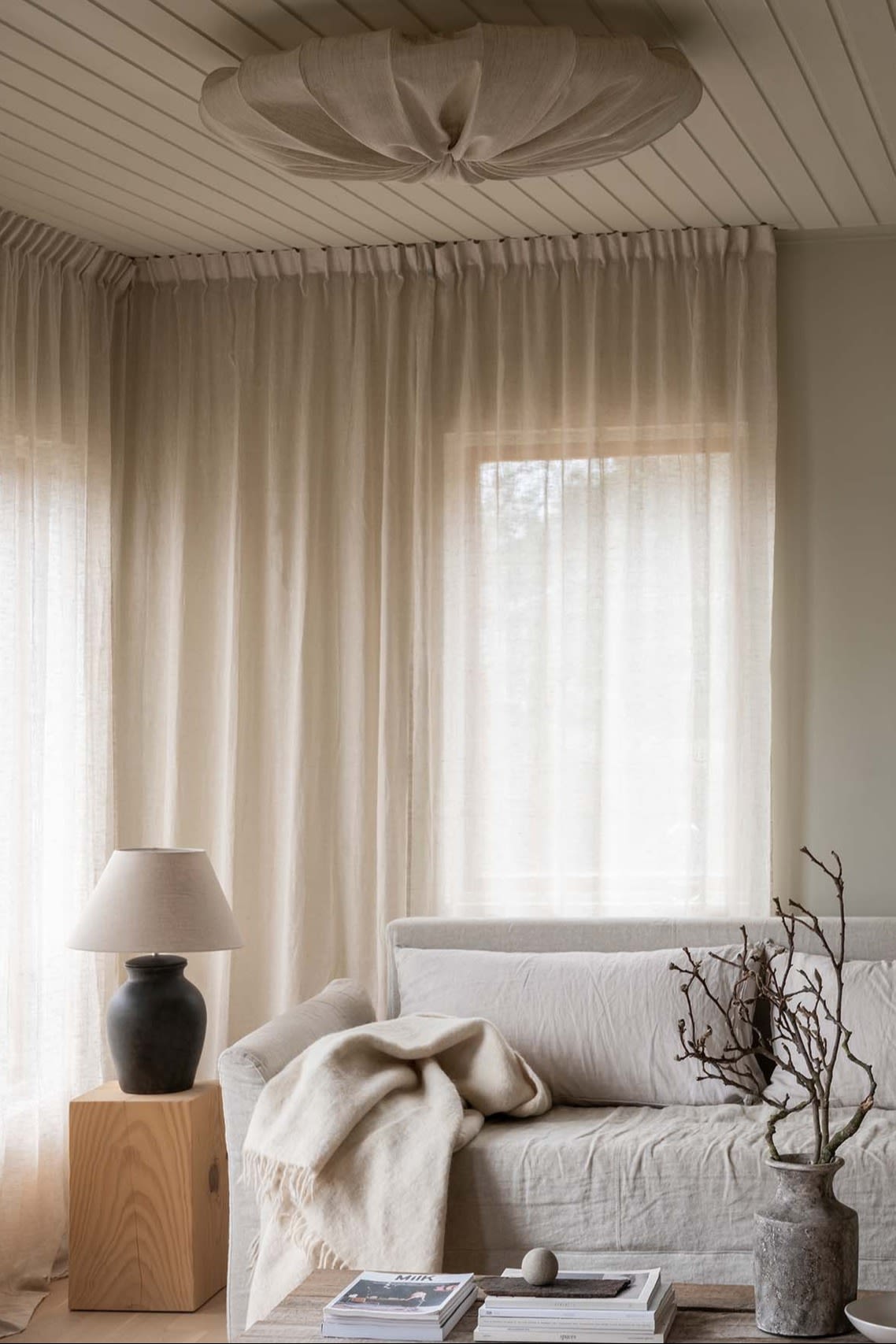 A bright living room with a beige sofa and light-coloured curtains, and a linen Anna ceiling from Watt & Veke.