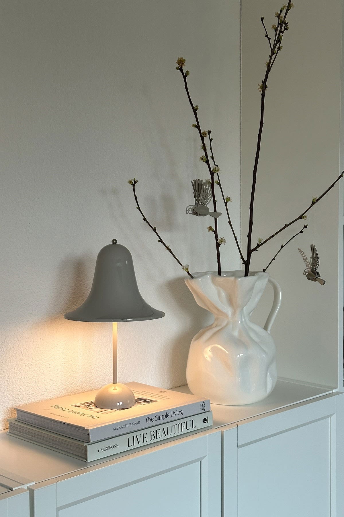 At @oursmall.home you can see two possible Mother's Day gifts: the Pantorp table lamp from Verpan stands on a chest of drawers, next to it the Crumple vase from Byon with a few twigs in it.