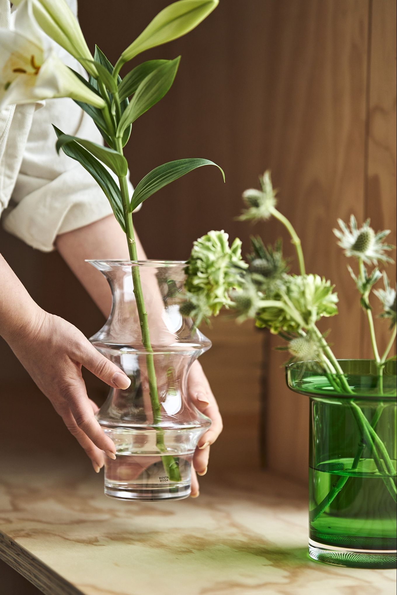 Hands place the Kosta Boda Pagod vase on a windowsill next to the green Limelight vase also from Kosta Boda. 