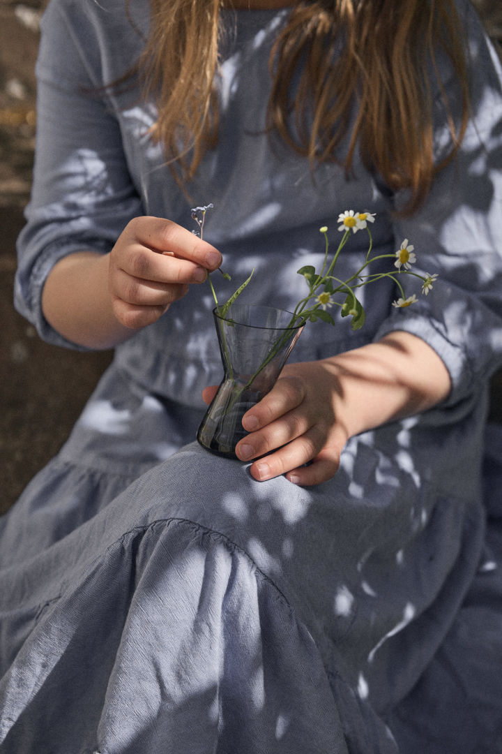 A young girl in a blue dress holding a mini vase from Orrefors.