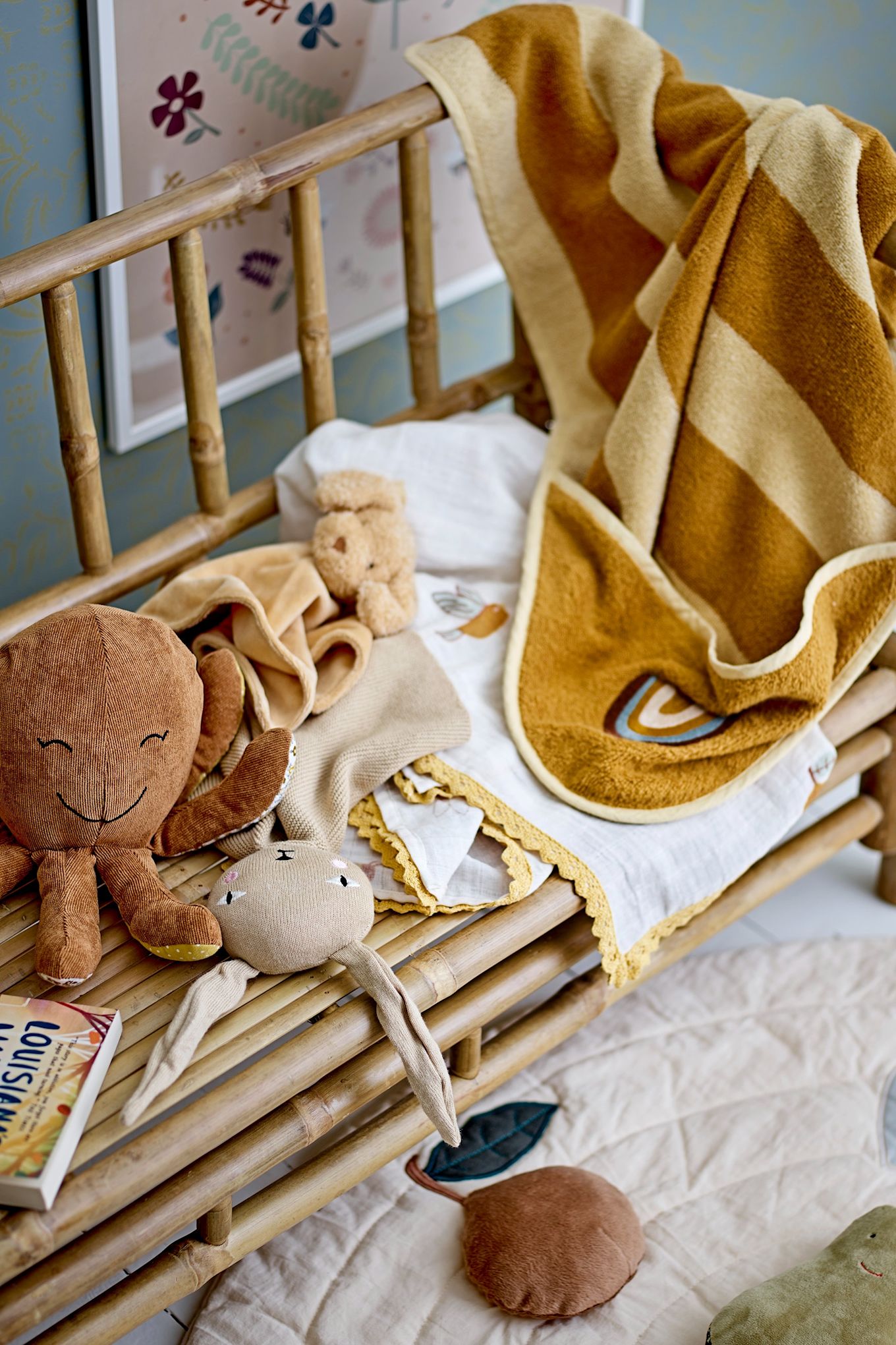 A yellow and brown hooded towel with a rainbow motif hangs over the arm of a bench with an octopus toy, the idea baby shower gift idea. 