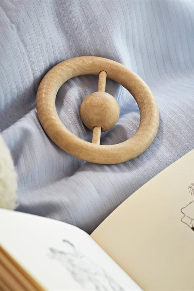 The ring rattle in wood from Kay Bojesen on a blue bed sheet, a rattle is a perfect baby shower gift idea. 