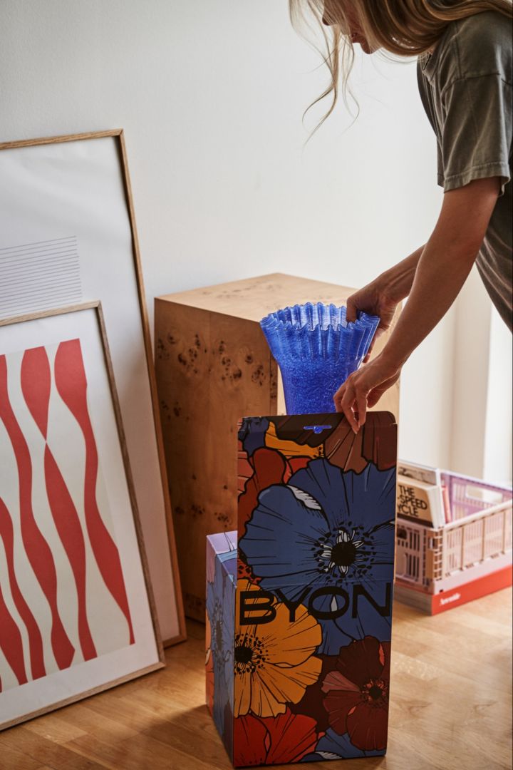 The blue Lori vase from Byon is a perfect addition to the autumn design trends 2024, seen here being placed into a colourful Byon box. 