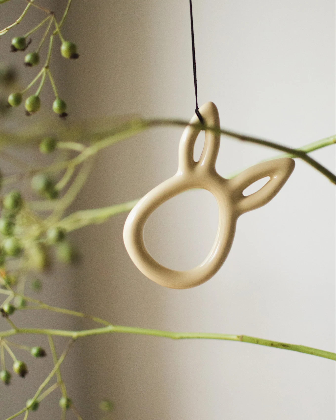 A light beige bunny-shaped ornament hangs among green branches with berries.