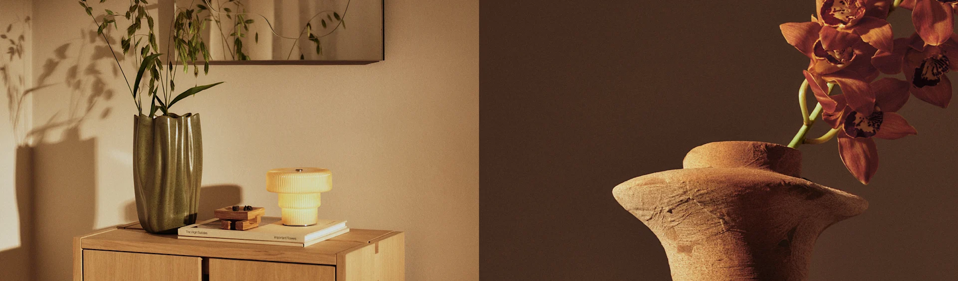 Two vases display plants, one green vase with foliage on a cabinet next to a yellow lamp, and one terracotta vase with orange orchids.