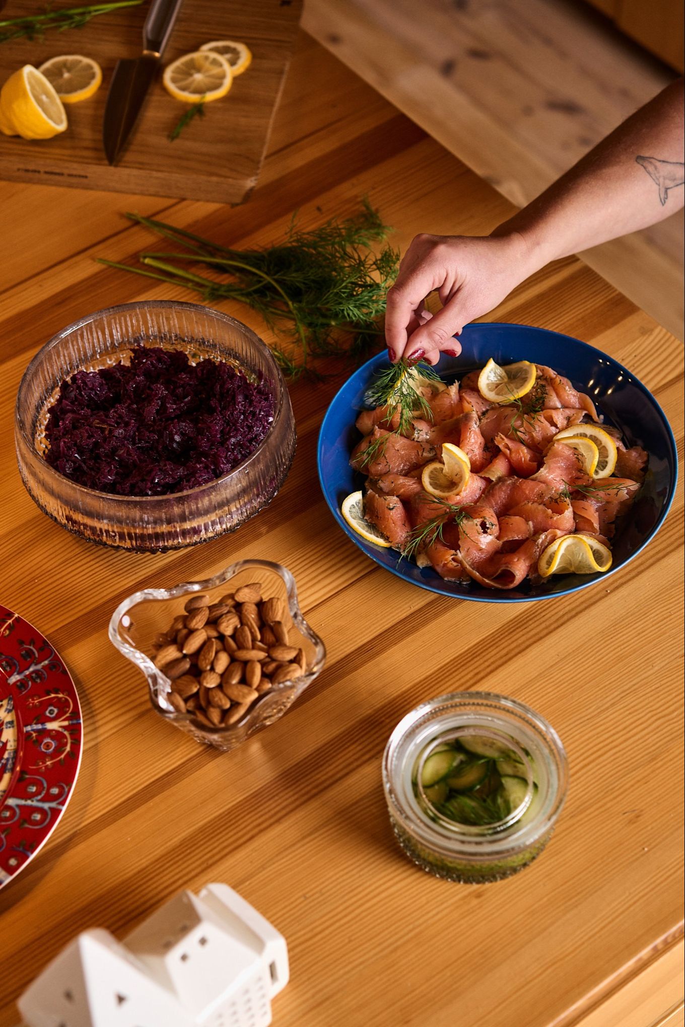 A hand places a piece of dill on a blue plate with salmon and lemon, a traditional dish as part of a Nordic Christmas celebration.