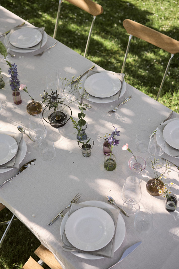 A white table setting with a centre piece of mini midsummer vases from Orrefors. 