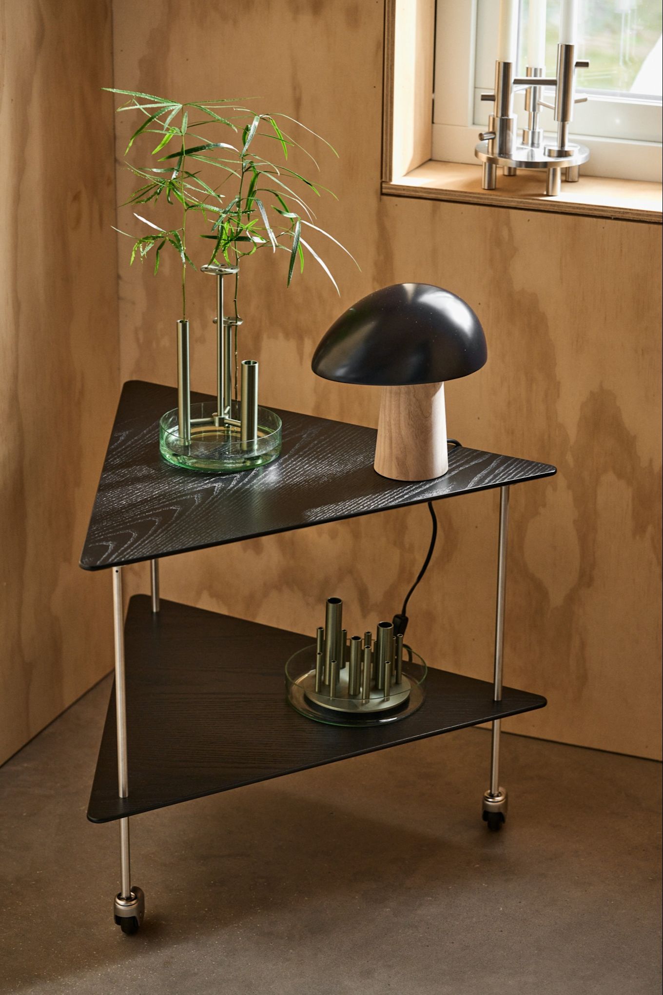 The AJ corner table in black stands in a plywood room with the Night Owl table lamp in midnight blue, the Ikeru vase and Jamie Hayon candle holder. All from Fritz Hansen. 