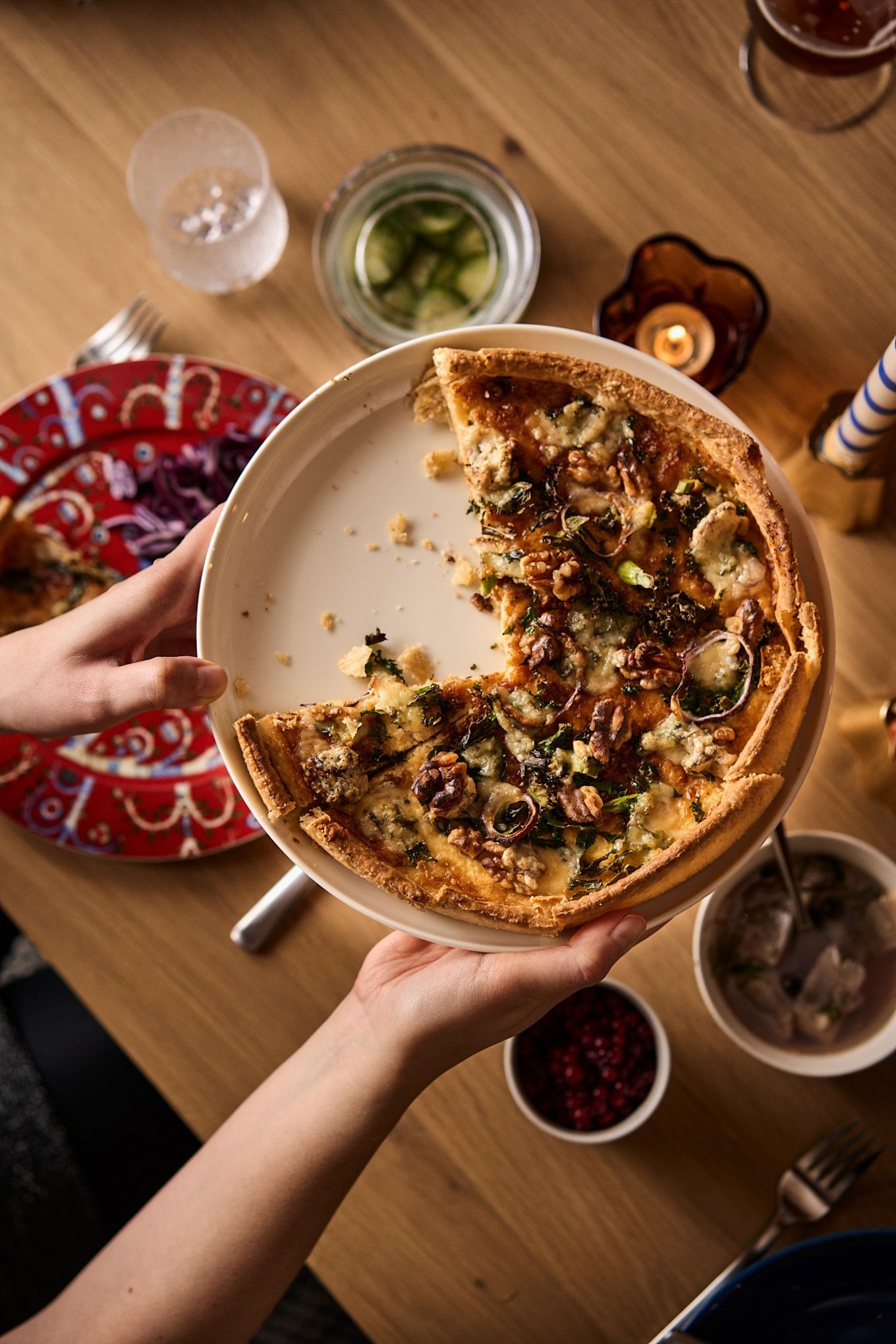 Hands hold a kale and cheese pie with a couple of slices missing, a traditional part of a Nordic Christmas celebration. 