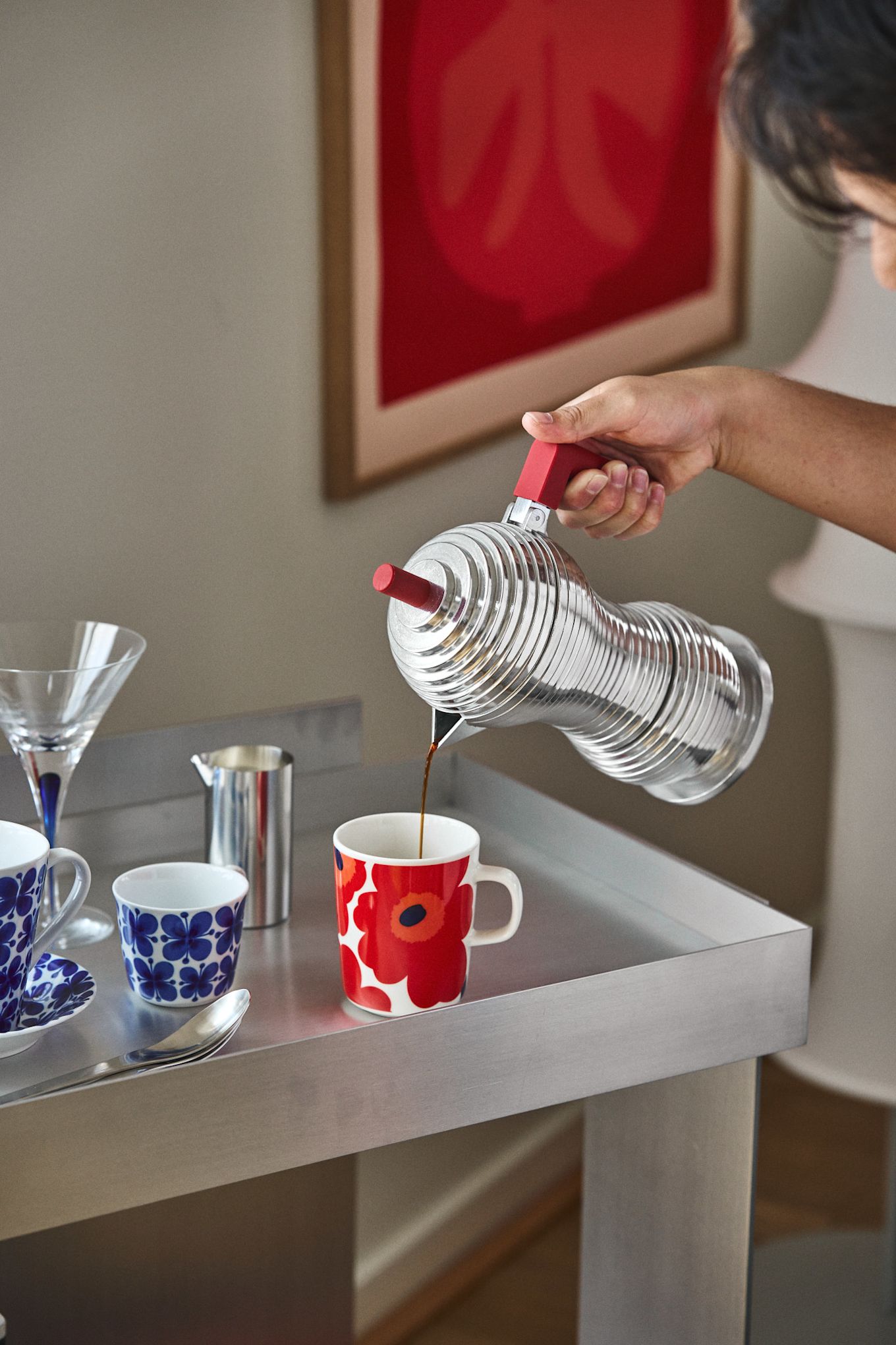 A good coffee bar also needs a suitable espresso maker. Here you can see a hand pouring coffee from the Pulcina espresso maker from Alessi into a cup from Marimekko.