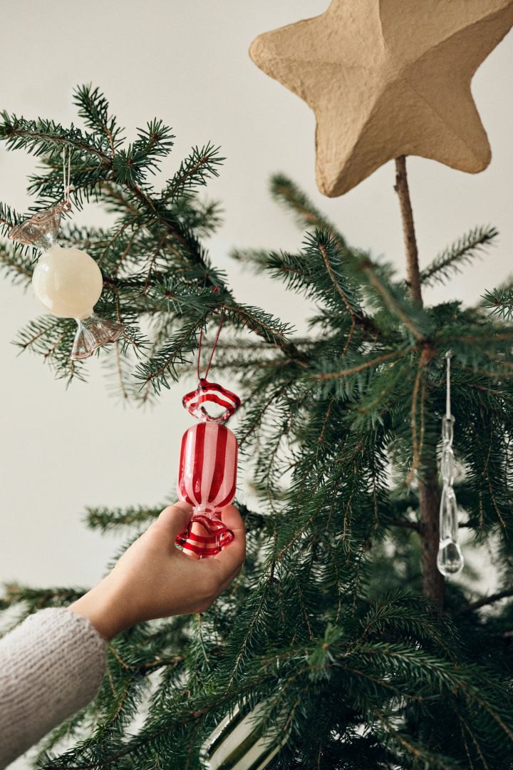 A hand places a large wrapped candy tree decoration into a Christmas tree a playful and colourful Christmas tree decoration idea. 