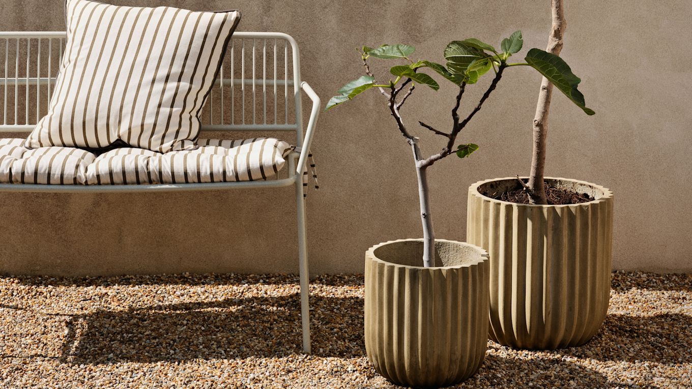 Here you see the Eden bench from Broste Copenhagen on a small balcony area with pots and trees in the sunshine. 