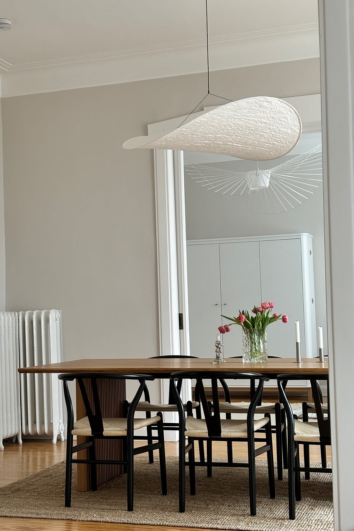 Update your home with modern lighting ideas, here you see the hanging ceiling lamp Tense from New Works  hanging over a dining table with a bunch of tulips. 