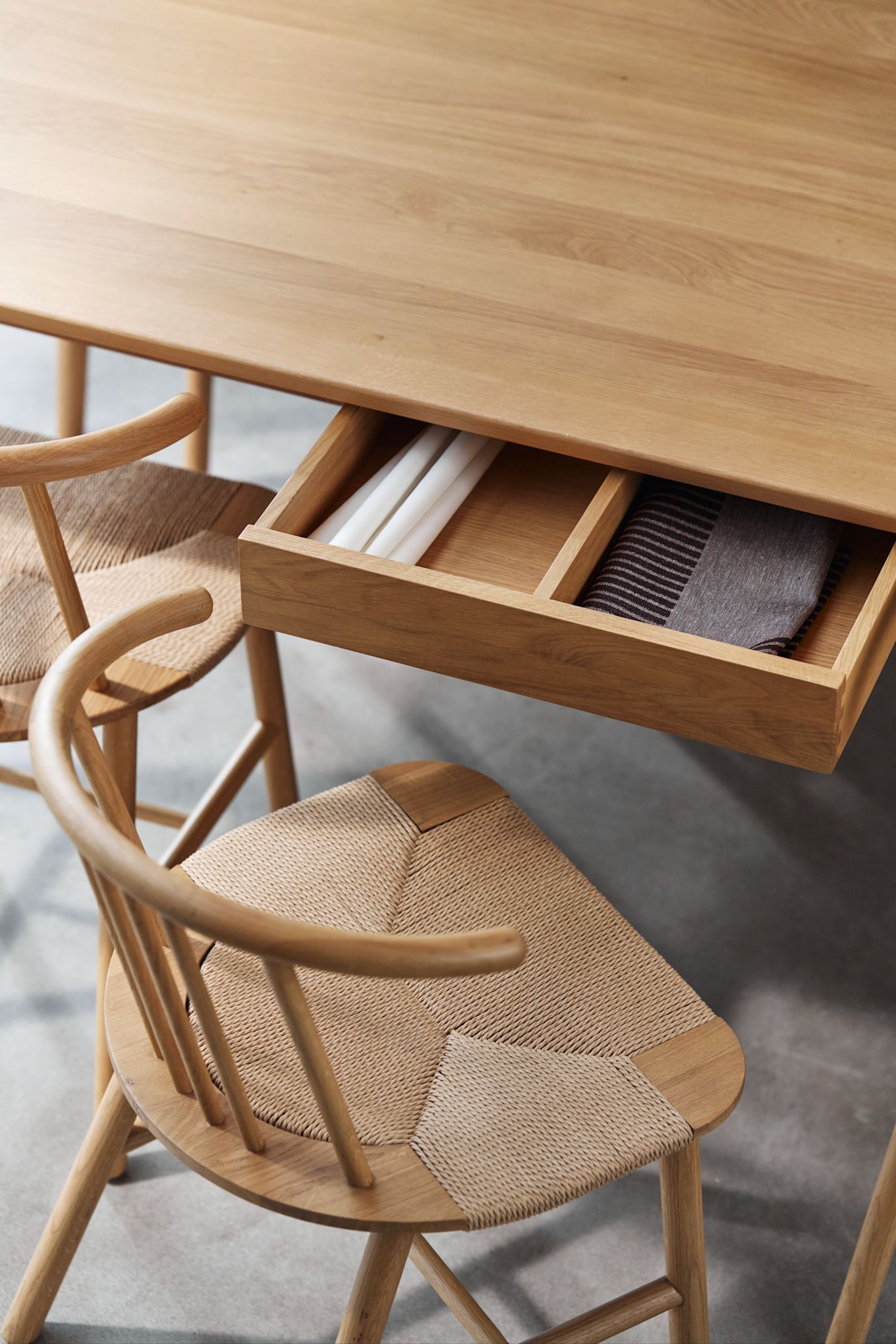 Scandinavian interior design trends 2025 - multifunctional furniture. Here, an oak table from NJRD with a pull-out drawer to store details.