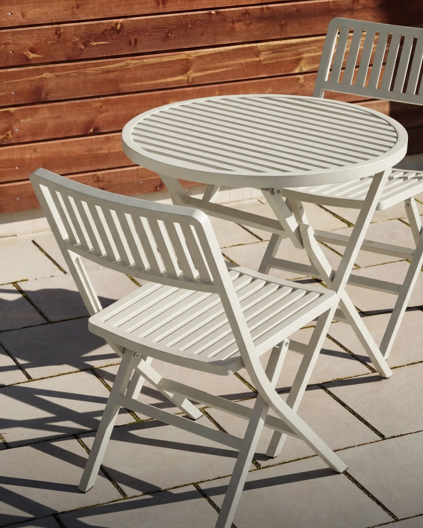 Light grey slatted outdoor table with two matching folding chairs on a patio.